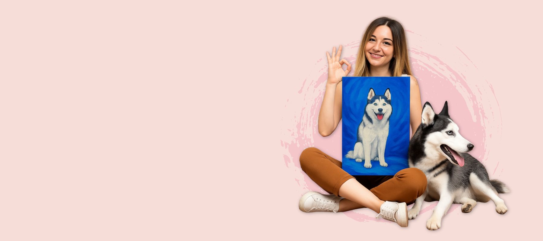 Woman holding a canvas painting of her dog, sitting on the floor with a dog next to her on a pink background