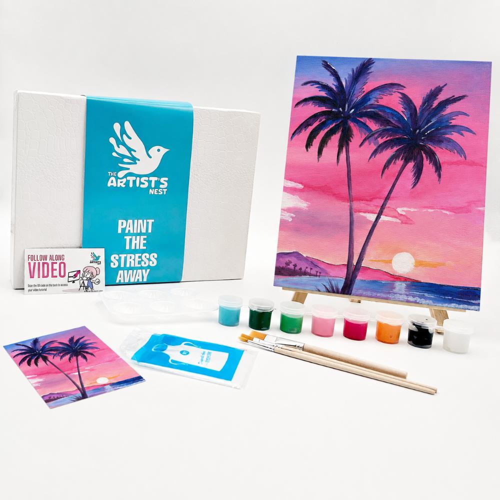 Painting kit by The Artists Nest, featuring a canvas with a painted tropical sunset scene, a white and teal instruction box, paint bottles, brushes, and a small sample card on a white background.