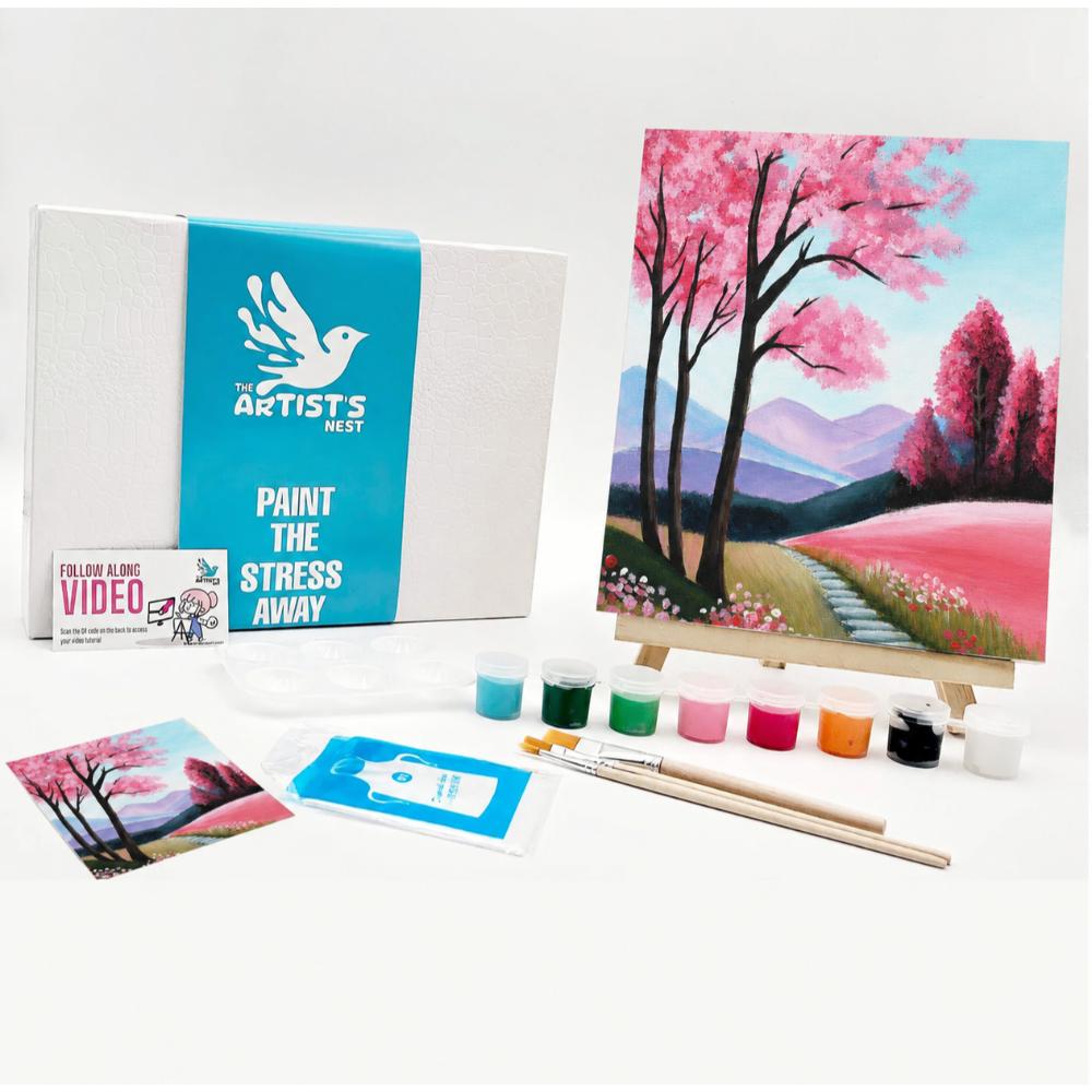Painting kit set displayed on a white background, including a canvas box with a turquoise label, a painted landscape artwork on an easel, paint tubes, brushes, a small instruction card, and a printed reference image.